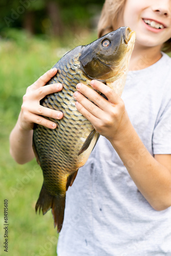 big fish carp in the hands of a boy, fishing with a child, a young fisherman, vertical photo