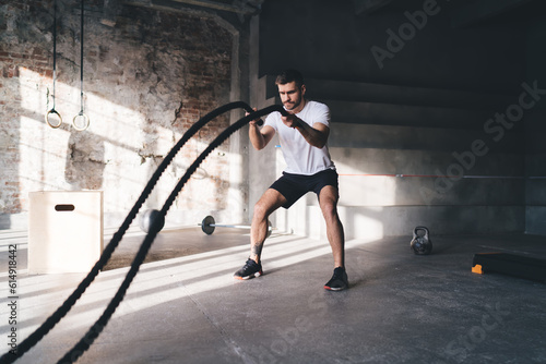 Strong man doing exercises with ropes in gym