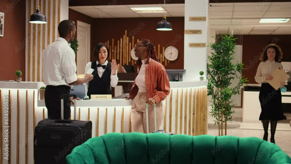 Friendly bellhop employee showing tourists the way to their room while carrying luggage after check in process is over. Stressed hotel manager verifying guests booking paperwork Friendly bellhop employee showing tourists the way to their room while carrying luggage after check in process is over. Stressed hotel manager verifying guests booking paperwork