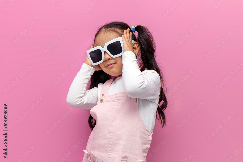 little girl preschool child in white sunglasses and pink sundress on a pink isolated background