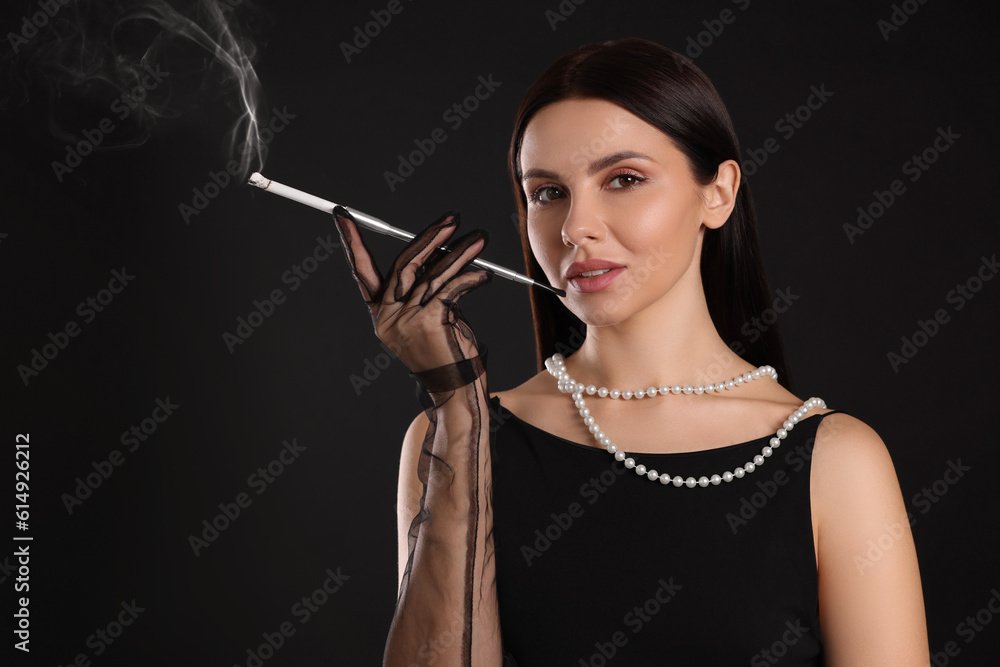 Obraz premium Woman using long cigarette holder for smoking on black background, space for text