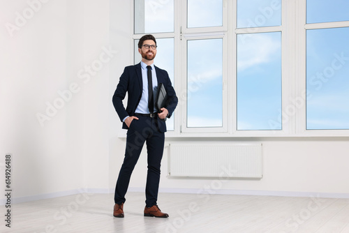 Handsome real estate agent with documents in empty room, space for text