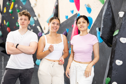Two young women in sportswear and teen guy posing against training wall at climbing wall