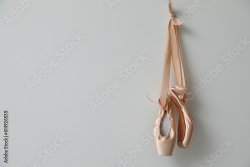 Beautiful beige ballet shoes with cute ribbons hanging on light grey wall. Space for text