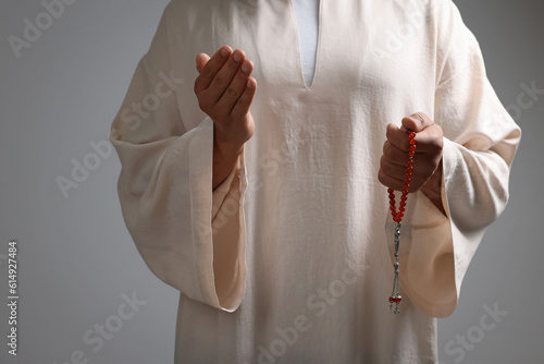 Muslim woman with misbaha praying on light grey background, closeup