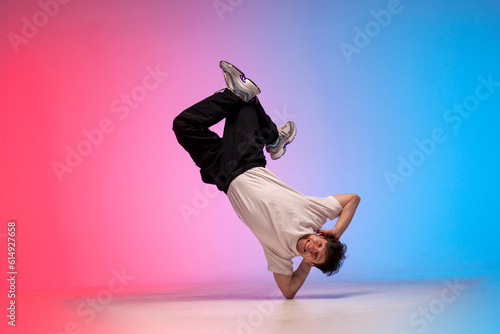 guy hiphop performer break dance in neon club lighting and doing acrobatic trick, male dancer stands in acrobatic pose