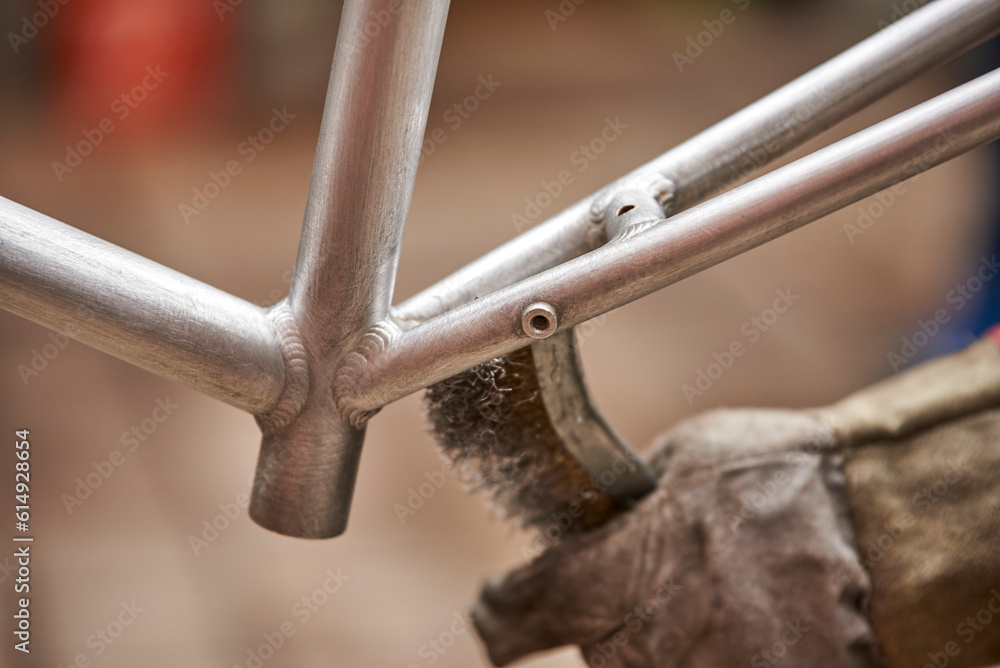 Unrecognizable man using a wire brush over a bicycle frame after passing a blowtorch over it to remove the paint, as part of his bike renovation work. Close up view. Unrecognizable man using a wire brush over a bicycle frame after passing a blowtorch over it to remove the paint, as part of his bike renovation work. Close up view.
