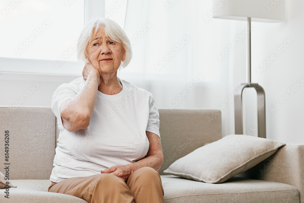 Elderly woman severe neck pain sitting on the sofa, health problems in old age, poor quality of life. Elderly woman severe neck pain sitting on the sofa, health problems in old age, poor quality of life.