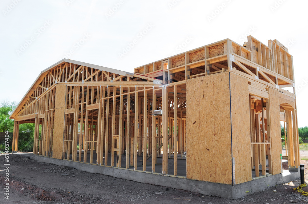 An exterior full view of the frame of a new wooden single-family home under construction showing its concrete slab 