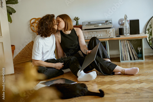 Young couple kissing while sitting on floor and listening music on vinyl player with records at home