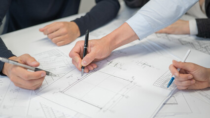 Close-up of the hands of four colleagues with blueprints on the table in the office. Brainstorming of engineers and architects.