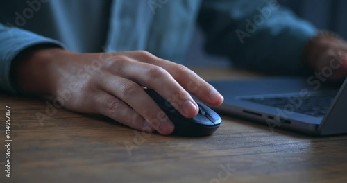 Close up man working on laptop computer, male hand uses a computer mouse in the evening. Male freelancer clicking black computer mouse while browsing internet or working on laptop at home office