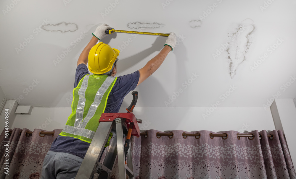 Water spots on ceiling being measured with tape measure by a man in a hard hat