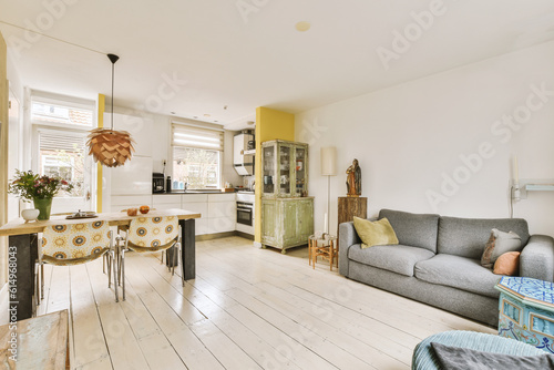 a living room with white wood flooring and yellow painted walls in the background, there is a grey couch