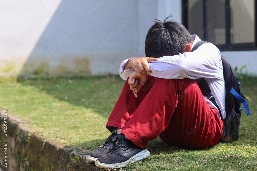 Sad young schoolboy sitting with hands on knees and head between his