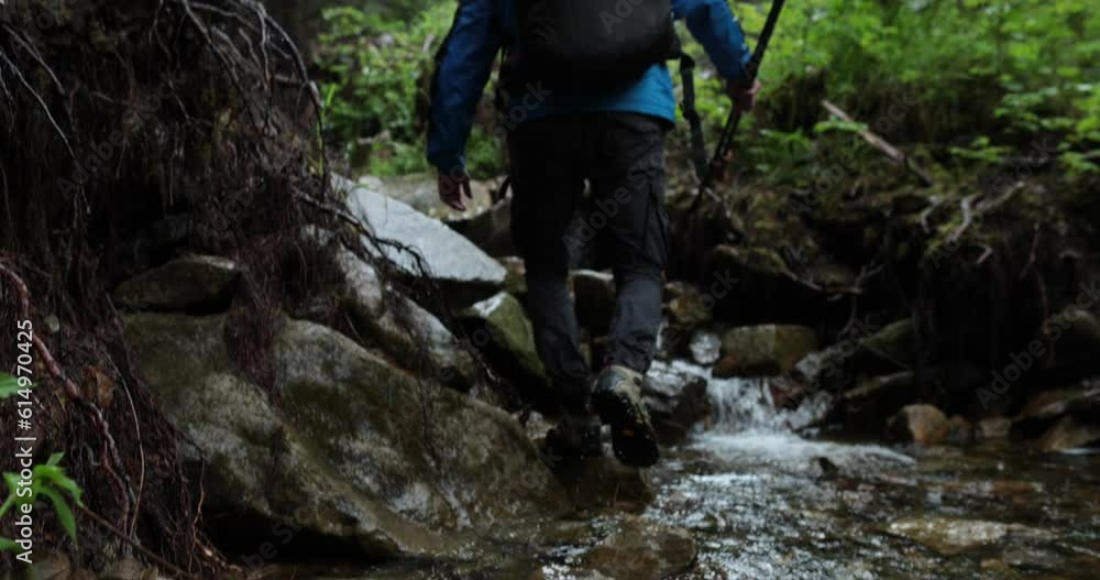 A man hiker walks through a mountain stream in the forest, walking on stones in the forest in rainy, wet weather. A man hiker walks through a mountain stream in the forest, walking on stones in the forest in rainy, wet weather.