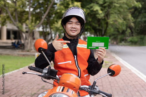 Happy young Thai motorcycle taxi driver or rider waiting for passenger near by the building in the city. photo