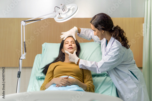 Female doctor or dermatologist examining facial skin of young patient prepare before facelift surgery. Atmosphere at cosmetic surgery department in hospital clinic.