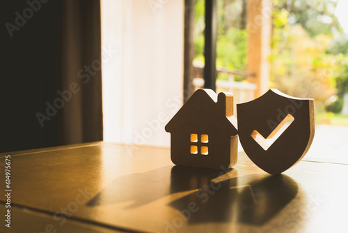 Wooden house model and real estate insurance ideas, and small shield icon. Housing insurance against impending loss and fire, building fire insurance concepts.