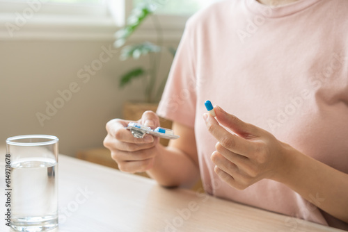 Sick, asian young woman, girl hand holding pill capsule, painkiller medicine from stomach pain, head ache, pain for treatment, take drug or vitamin and glass of water at home, pharmacy and health care photo
