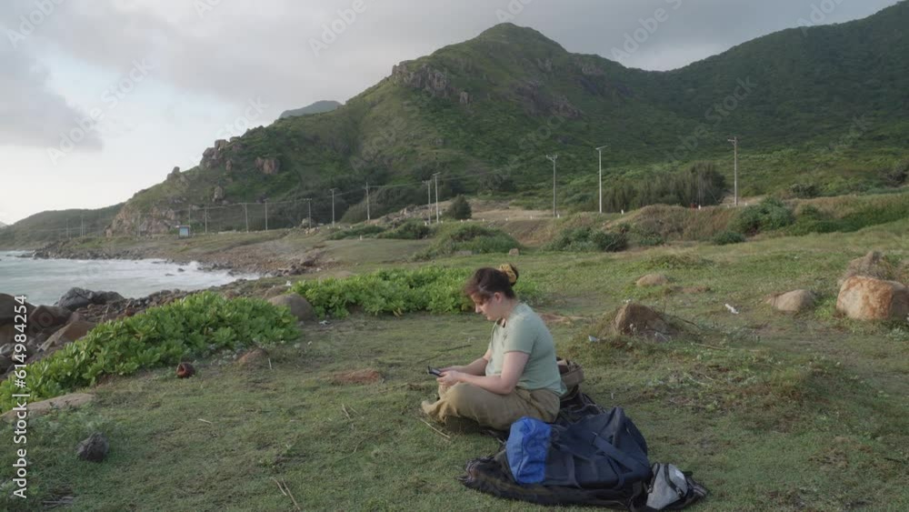 Woman Sitting on the sea shore reading book on Kindle device In Con Dao Island, Vietnam. Wide Shot Woman Sitting on the sea shore reading book on Kindle device In Con Dao Island, Vietnam. Wide Shot