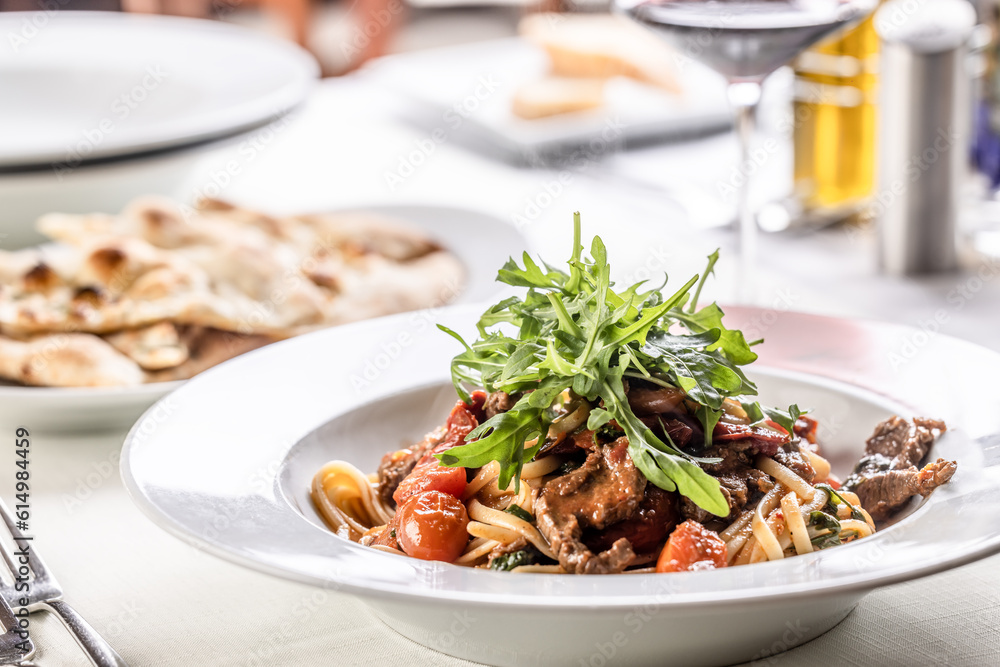 Linguine with tomatoes and tender beef meat served in a plate and topped with rocket salad