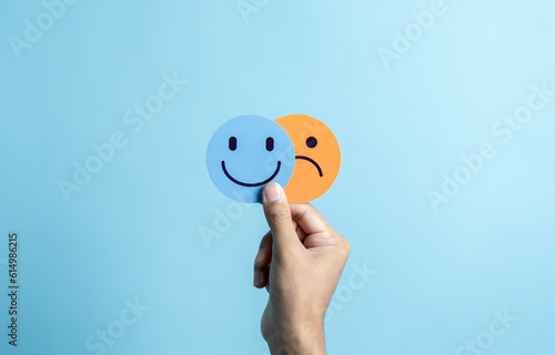 Hands holding sad face hiding or behind happy smiley face, bipolar and depression, mental health concept, personality, mood change, therapy healing split concept. photo