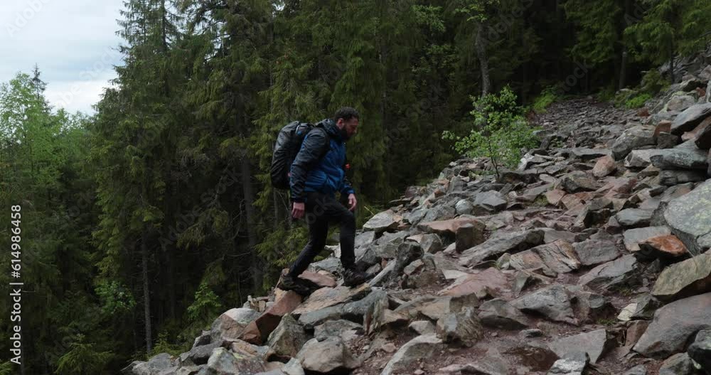 A man is a hiker on a hike in a mountain forest walking on rocky terrain in cloudy weather. Single hikes in the mountains. A man is a hiker on a hike in a mountain forest walking on rocky terrain in cloudy weather. Single hikes in the mountains.