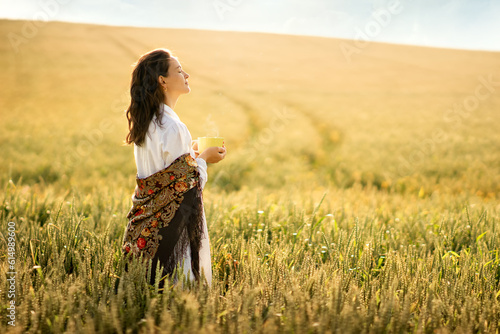 a young woman of white race, brown-haired,she went out at dawn to a wheat field to drink a cup of tea,coffee,she is wearing a white nightgown and a colored shawl,an atmosphere of calm,love,air,freedom