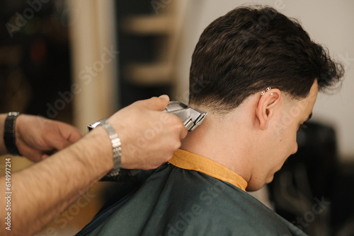 Barber use trimmer to cut hair of man. Back view of male client sitting 