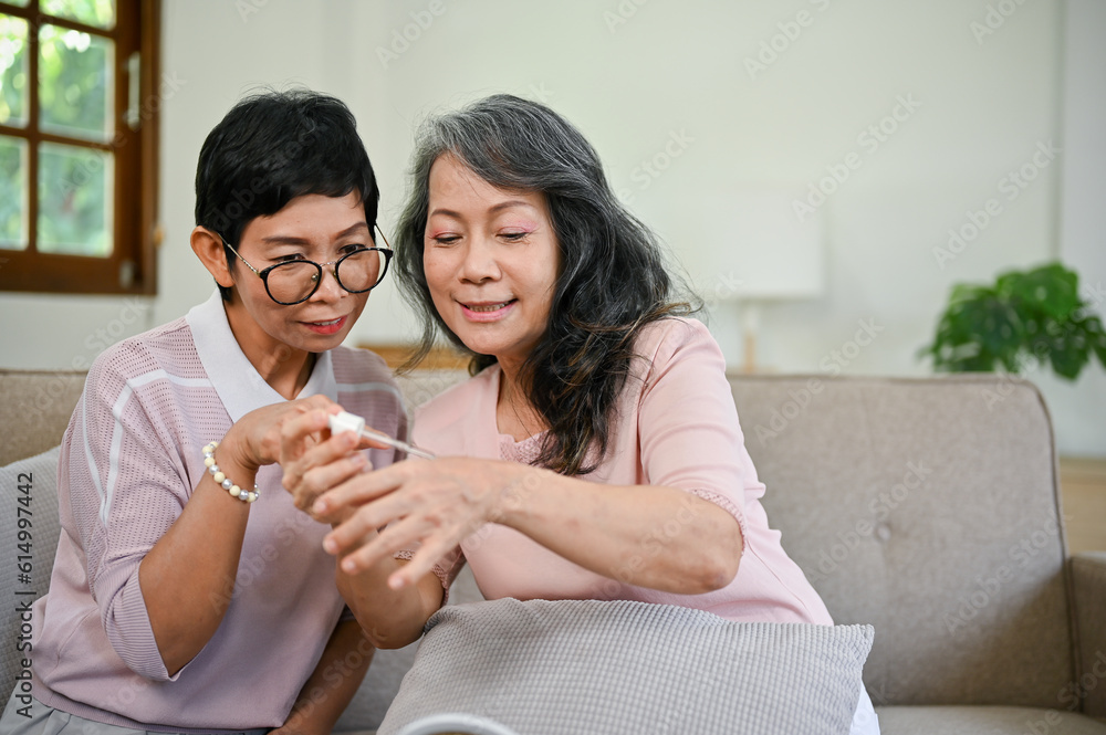 Two happy middle-aged Asian female friends are trying new makeup products in the living room Two happy middle-aged Asian female friends are trying new makeup products in the living room