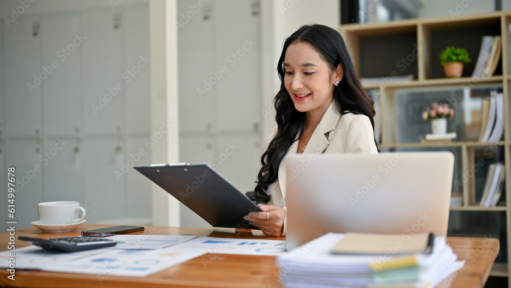 An attractive Asian businesswoman is reading business reports at her desk in the office. An attractive Asian businesswoman is reading business reports at her desk in the office.