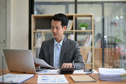 A professional Asian businessman focuses on business financial reports, working at his desk