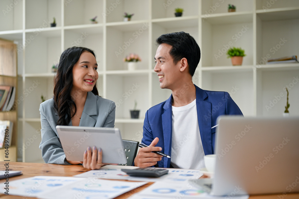 A smiling Asian businessman enjoys talking and working with a female colleague A smiling Asian businessman enjoys talking and working with a female colleague
