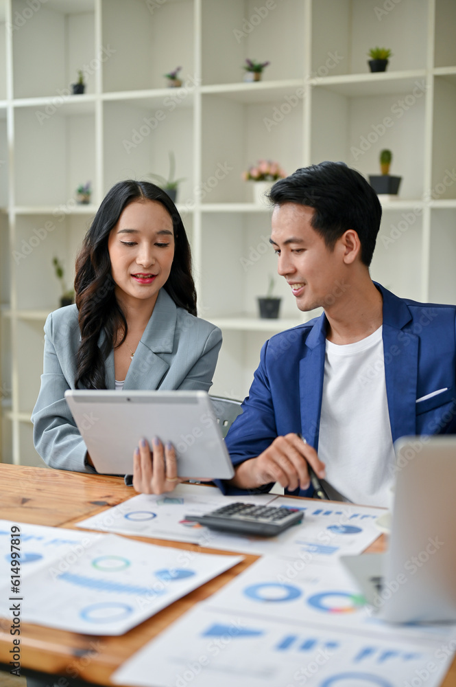 A businesswoman and a businessman are looking down at a tablet screen, discussing ideas A businesswoman and a businessman are looking down at a tablet screen, discussing ideas