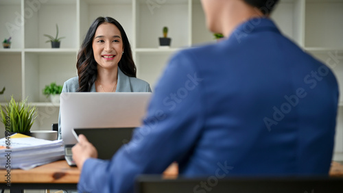 A smiling Asian businesswoman is working with a male colleague in the office.