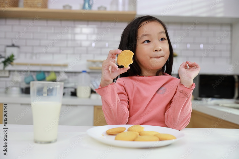 Kid asian black hair girl sitting on table and drinking milk while eating vanilla cookies for breakfast with enjoying time. Tasty food and delicious food with happy meal lifestyle kid concept