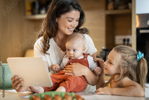 Little girl looking at tablet for breakfast recipe while her mother holds her baby sister 