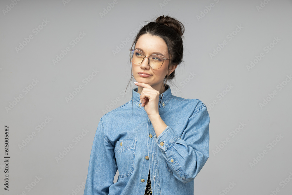 A young woman in glasses thinks on a gray background A young woman in glasses thinks on a gray background