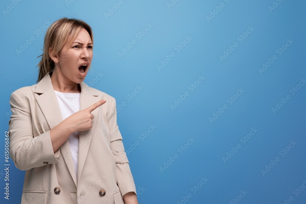 surprised blond young woman in jacket pointing finger to side on studio background surprised blond young woman in jacket pointing finger to side on studio background