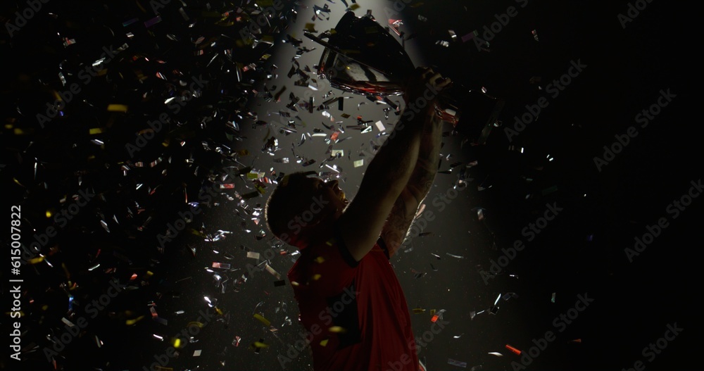 Silhouette of Caucasian male rugby player raising a trophy above head against bright light and falling confetti. Super slow motion, shot on RED cinema camera