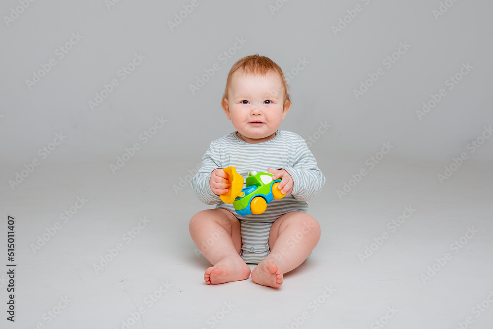 Cute toddler boy 10 months old in white bodysuit plays with car toy sitting on a white background, space for text Cute toddler boy 10 months old in white bodysuit plays with car toy sitting on a white background, space for text