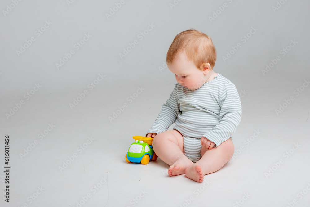Cute toddler boy 10 months old in white bodysuit plays with car toy sitting on a white background, space for text Cute toddler boy 10 months old in white bodysuit plays with car toy sitting on a white background, space for text
