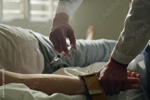Photography Close-up of doctor of lunatic asylum making injection to young male patient with