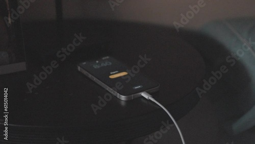 Mobile phone alarm going off on the nightstand. Charging cell phone alarm clock that sounds and anonymous hand that deactivates it. photo