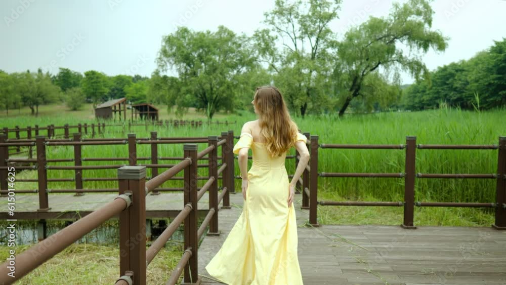 Stylish woman in yellow dress walking in slow motion on wooden planks in outdoors Stylish woman in yellow dress walking in slow motion on wooden planks in outdoors