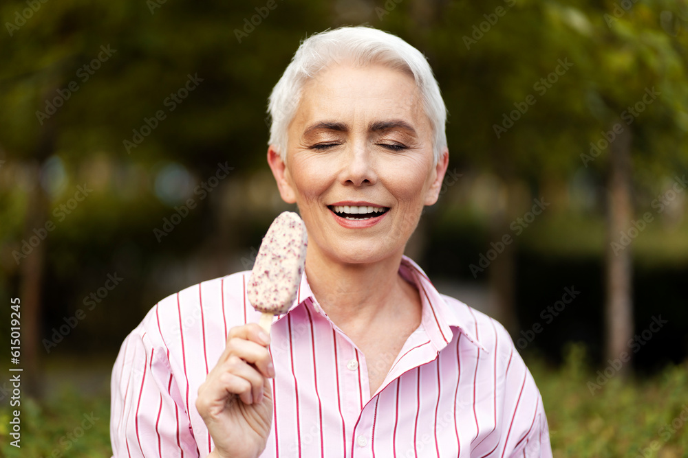 Portrait of smiling stylish gray haired woman eating tasty ice cream with close eyes standing in park. Summer positive lifestyle concept Portrait of smiling stylish gray haired woman eating tasty ice cream with close eyes standing in park. Summer positive lifestyle concept