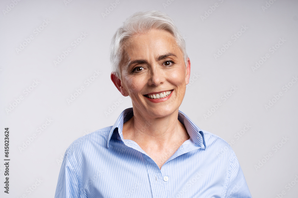 Portrait of smiling senior woman, wearing stylish, casual shirt, looking at camera isolated on gray background. Confident middle aged female posing for picture in studio Portrait of smiling senior woman, wearing stylish, casual shirt, looking at camera isolated on gray background. Confident middle aged female posing for picture in studio