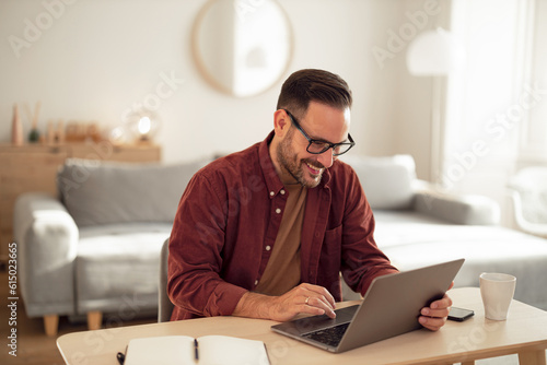 Smiling man typing an email, working from home office.