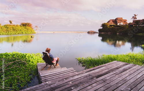 Canvas Print man with hat sitting calmly in front of a landscape in front of the river water